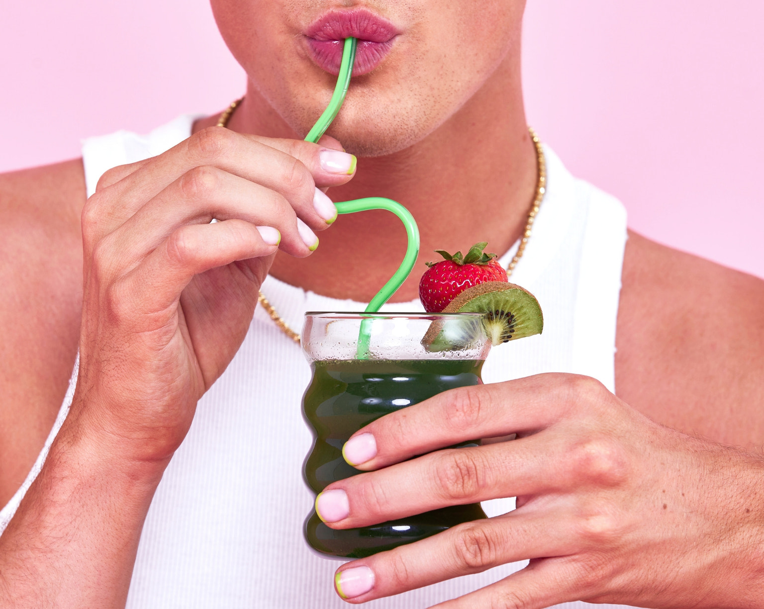 Person sipping Bloom Greens & Superfoods Strawberry Kiwi drink with curly straw, kiwi and strawberry garnish
