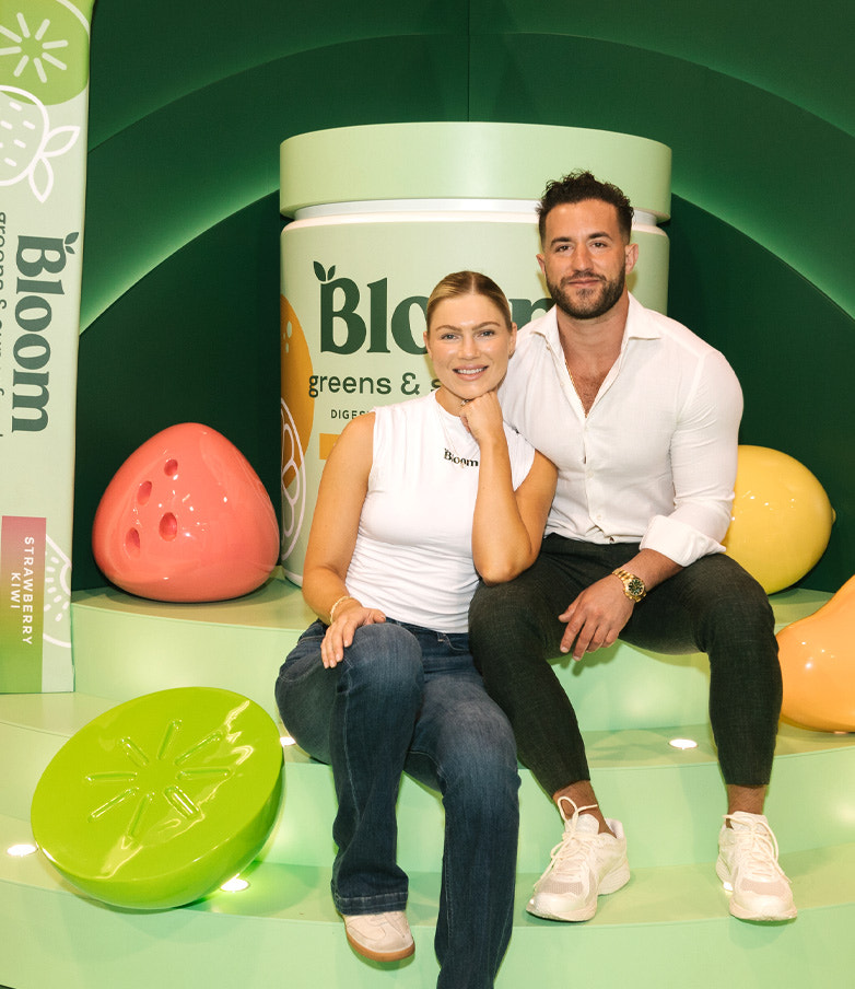 Mari and Greg, Bloom co-founders, seated in front of oversized greens & superfoods display